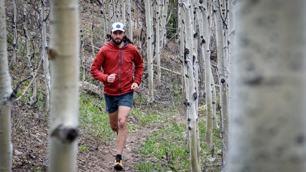 Trail runner in a lightweight red shell moving through aspens.